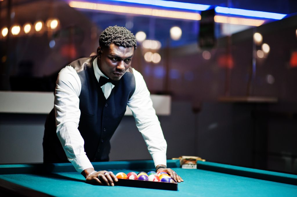 Young handsome african man wearing white shirt, black vest and bow tie play pool billiard.